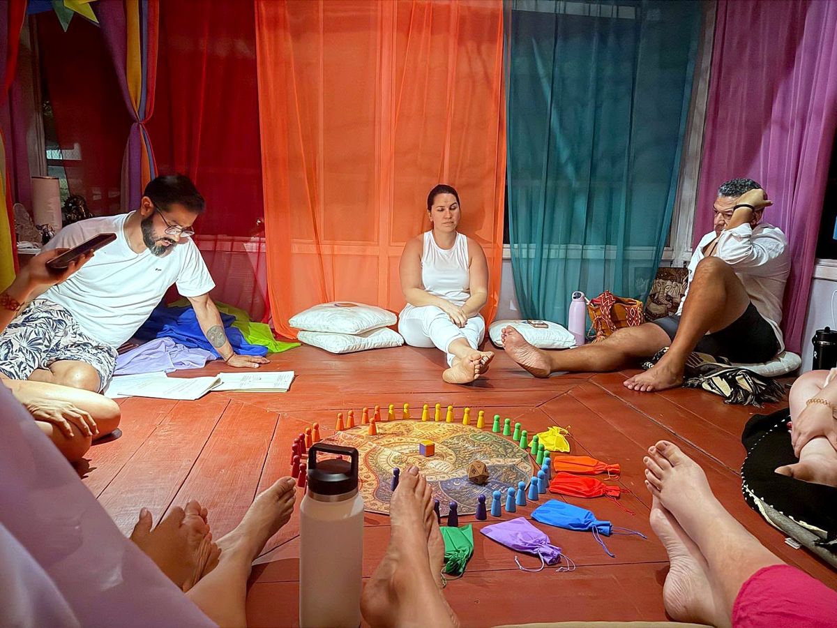 Adults sitting on the floor around the Familias de Colores board, surrounded by colored fabric