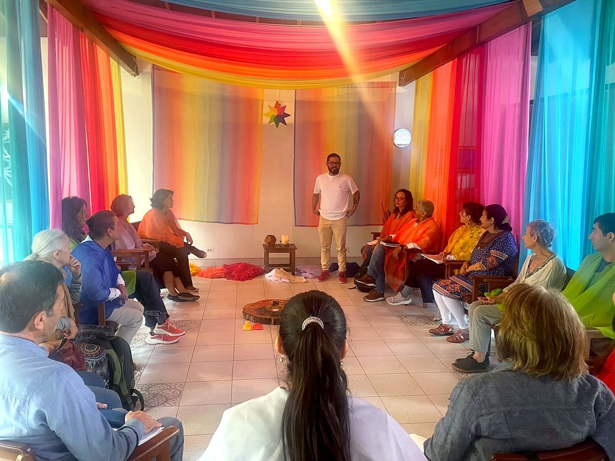 Adults sitting in a circle in a room draped in rainbow fabric at the start of the gathering